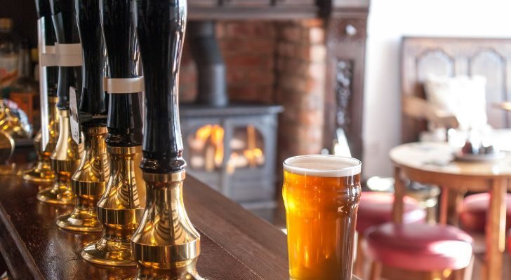 A view of the inside of a British pub, with taps for real ale and a glass of ale on the counter. In the background a fireplace can be seen