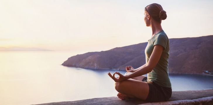 A woman in meditation pose looking out across the sea.