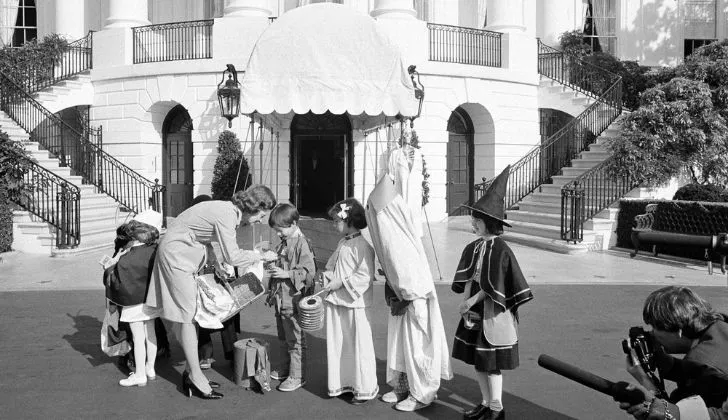 A black and white photo showing children dressed Halloween costumes outside the White House