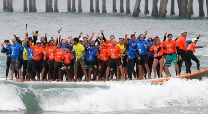 66 people on one big surfboard riding a wave