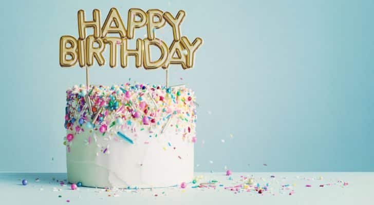 A modern birthday cake covered in white icing and candles on top