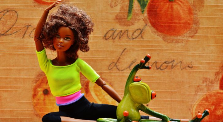 A Barbie doll and a ceramic frog posed like they're exercising.