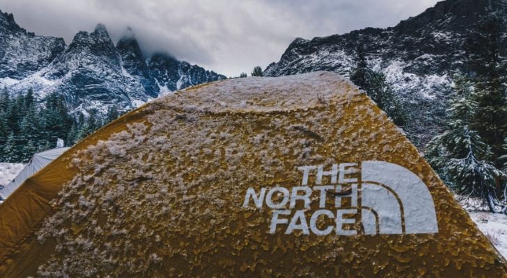 A North Face tent covered in snow, with snowy mountains in the background