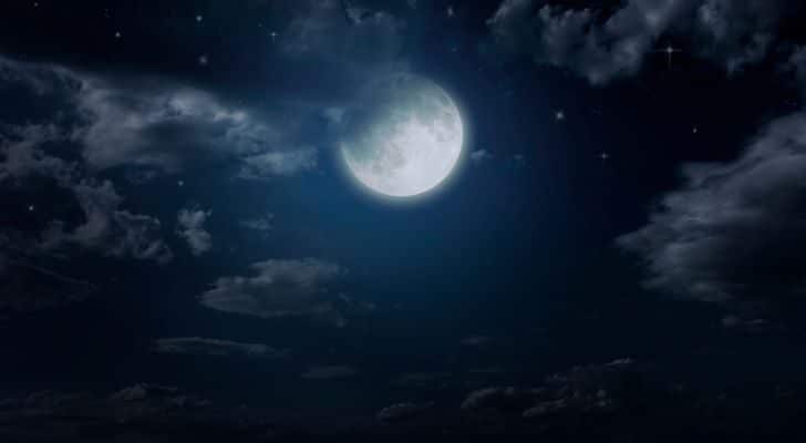 A pale moon lights up part of the night sky through the clouds