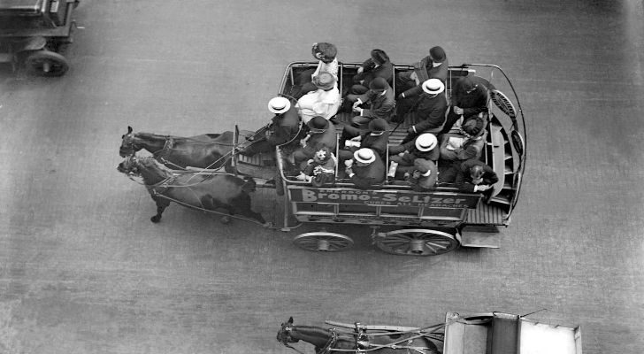 A black and white photo of an old horse-drawn bus with passengers in