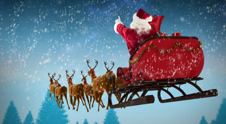 Santa rides his sleigh through a snowy sky led by flying reindeer