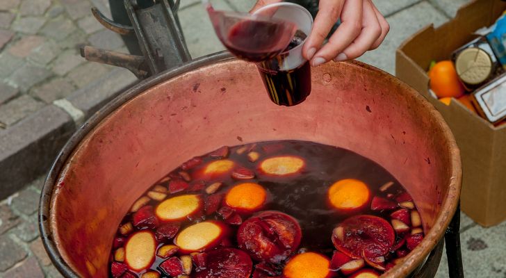 A cup is poured from large pot of mulled wine with fruit floating in it