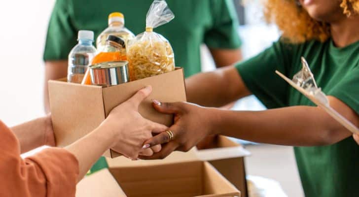 A woman hands a box off various food goods to someone else