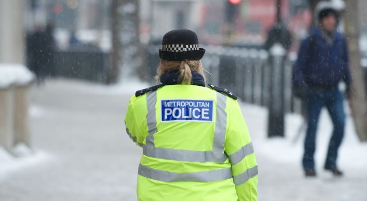 A female police officer in a high visibility jacket walks away through a street