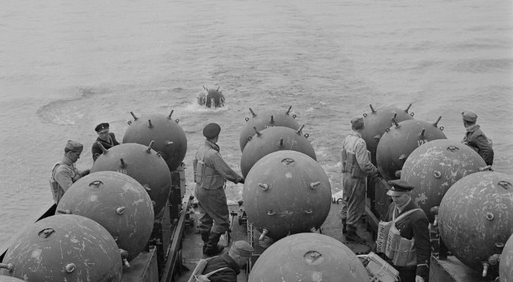 A boat with a large supply of sea mines deploys them to the ocean while sailing