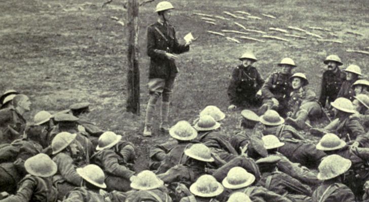 A group of Allied soldiers lie on the ground and receive instructions from a superior officer