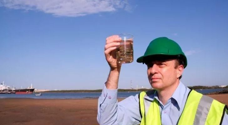 A person inspecting a sample on a beach