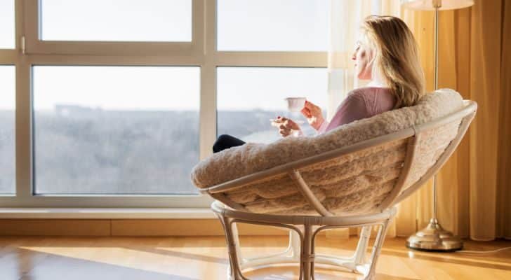 A woman sits peacefully in a chair and looks out of a window while sipping a coffee