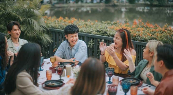 A group of friends laughs together around a table of food