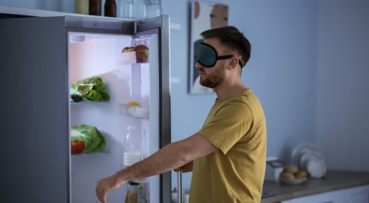 A man sleepwalking to the fridge while wearing an eye mask