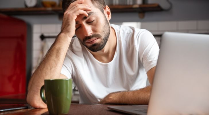 A man with a laptop and coffee looking very tired