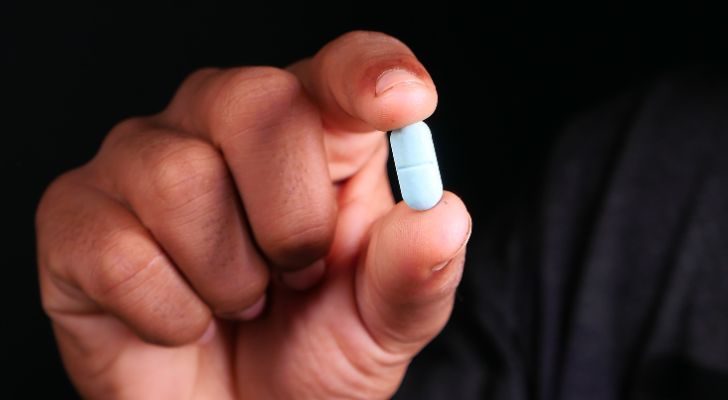 A person's hand holding a bright blue pill