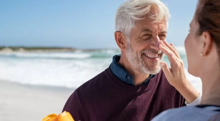 A woman applying sunscreen to an elderly man