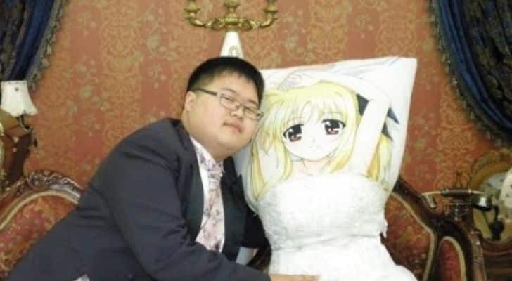 A man sitting next to a human-sized pillow that is inside a wedding dress