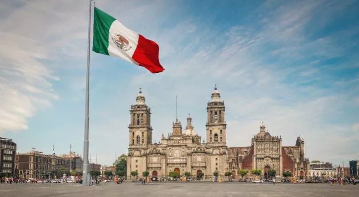 A Mexican plaza in front of a cathedral with a large Mexican flag flying