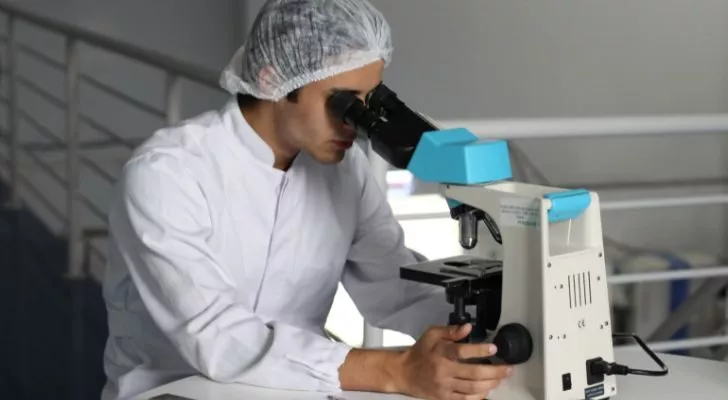 A scientist in white lab clothes using a microscope