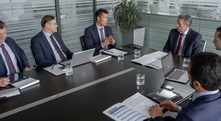 A boardroom of men in suits and ties discuss business