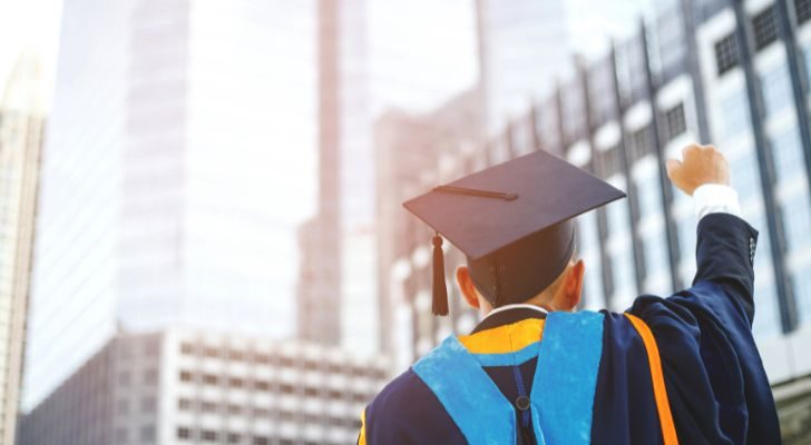 A man wearing academic regalia punching his fist into the air to celebrate