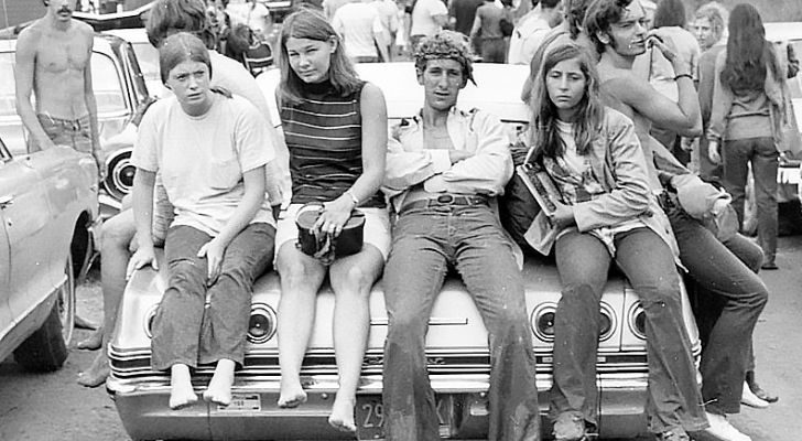 A group of young baby boomer hippies sitting on a car