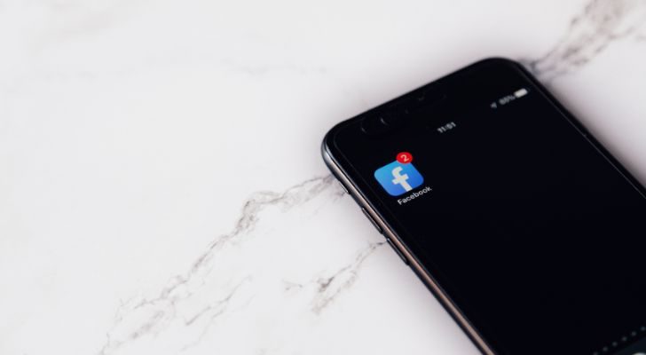 An iPhone lying on a marble countertop with a Facebook icon showing on the screen