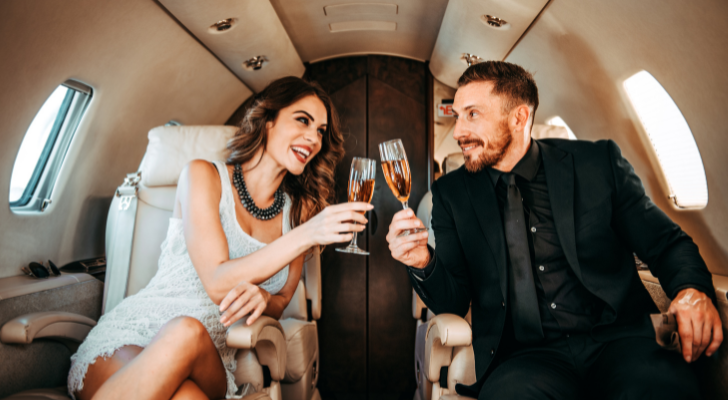 A wealthy looking couple toasting their drinks on a private plane
