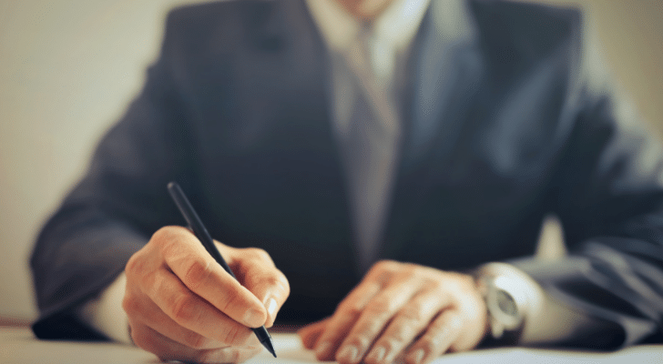 A man in a suit sitting at a desk signing papers