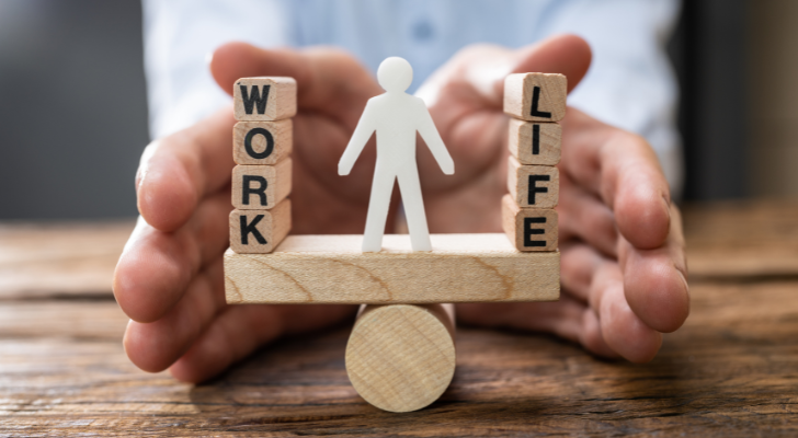 Small wooden blocks with the words "work" and "life" balanced on either side of a small human cutout