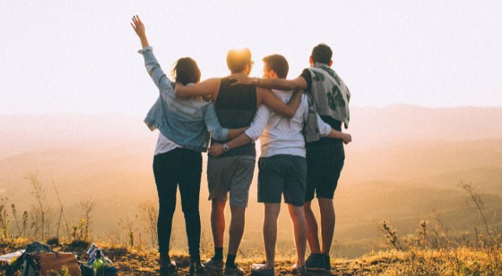 Four friends embracing each other just before sunset while looking out into the distance