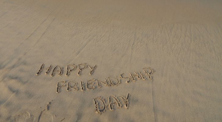 The words "Happy friendship day" written in the wet sand of a beach