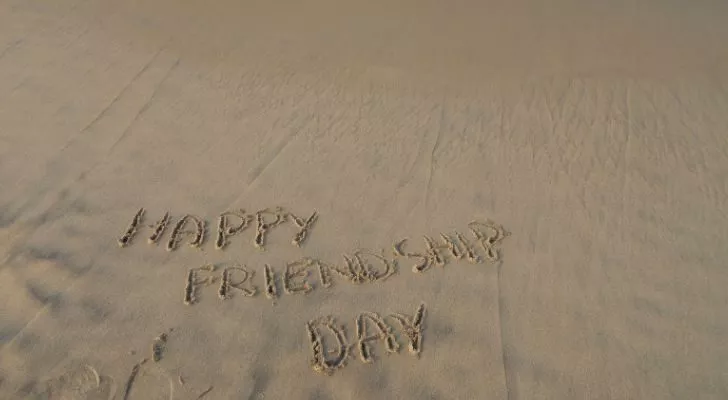 The words "Happy friendship day" written in the wet sand of a beach