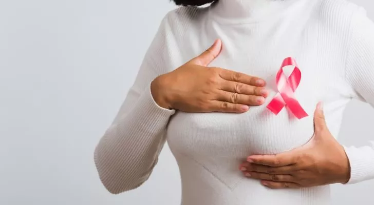 A woman in a white sweater with a pink breast cancer awareness ribbon inspects her breast