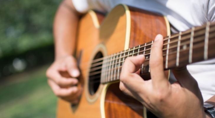 A man playing a guitar outside in the sun