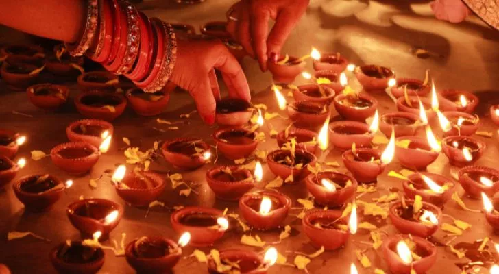 Two people lighting many small candles by hand for the Diwali festival