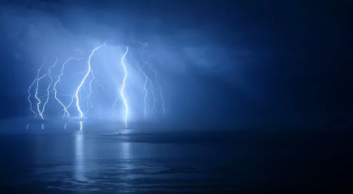 Streaks of lightning shooting out of a mass of clouds and into the sea