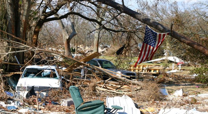 A house destroyed by a hurricane with an American flag hanging amongst the wreckage