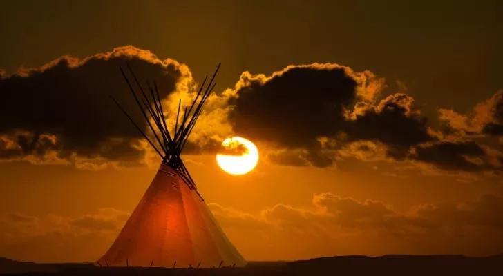 A First Nation teepee in a field, backed by an autumn sunset