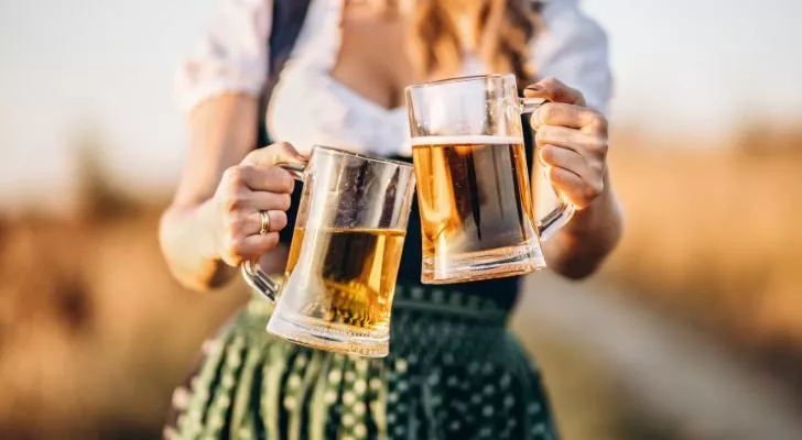 A woman in traditional Oktoberfest attire holds up two steins of beer