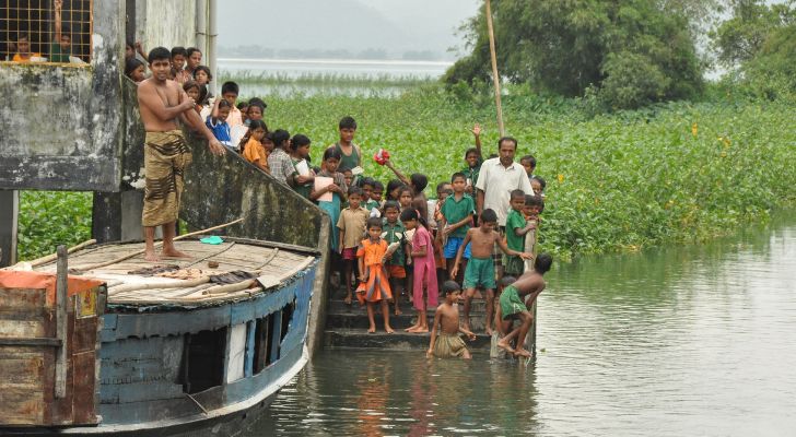 A group of Bangladeshi children standing next to a floating classroom