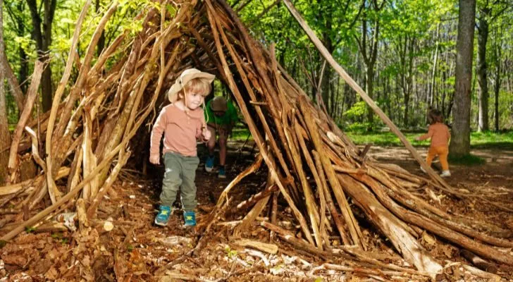 A child playing in the woods in a small shelter built out of sticks