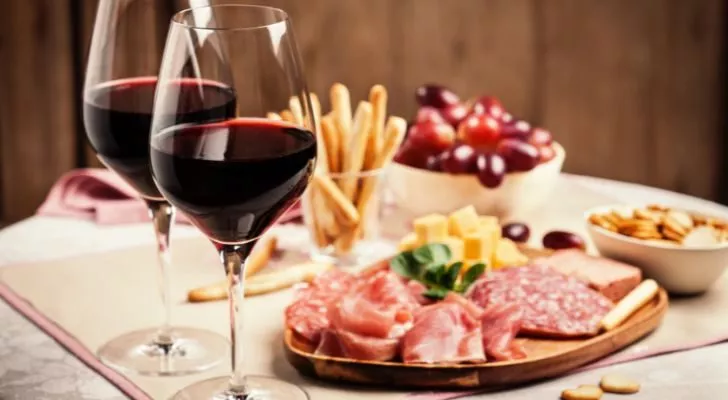 Two glasses of red wine with charcuterie, cheese, grapes and snacks