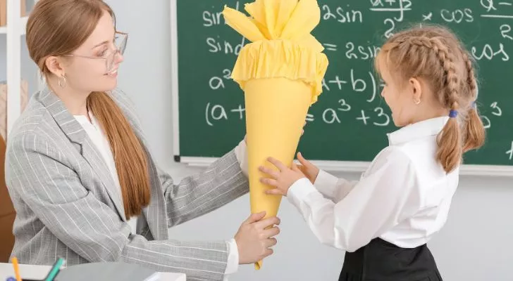 A teacher handing a child a large cardboard cone decorated in yellow