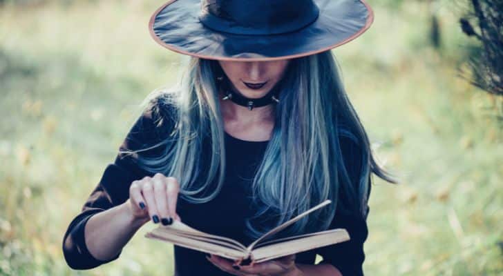 A woman dressed as a witch reading from a book in nature