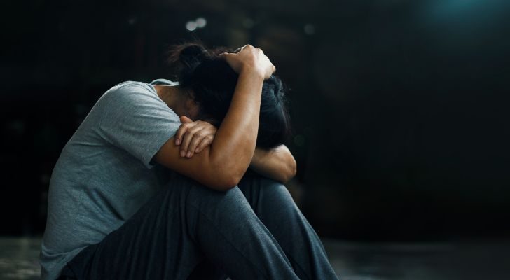 A person sitting in the shadows holding their head