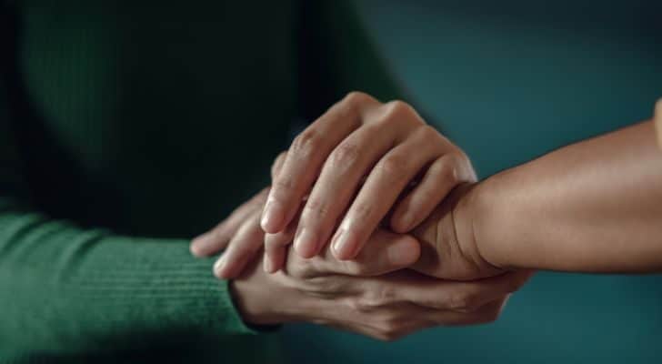 A person wearing green gently holds the outstretched hand of someone else