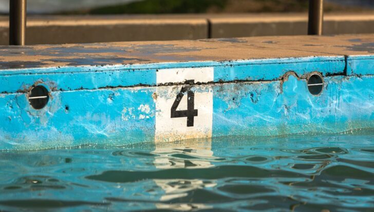 Number 4 painted on a worn blue poolside wall above water